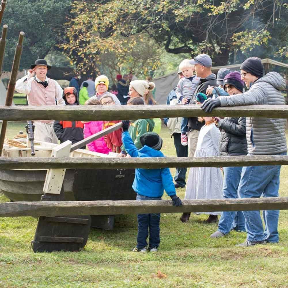 Visitors Surrounding a Wooden Boat at an Encampment Event